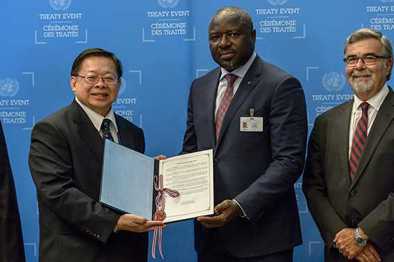 Three men in suits pose for the photo: Two hold the ratification document, the third is a bystander.